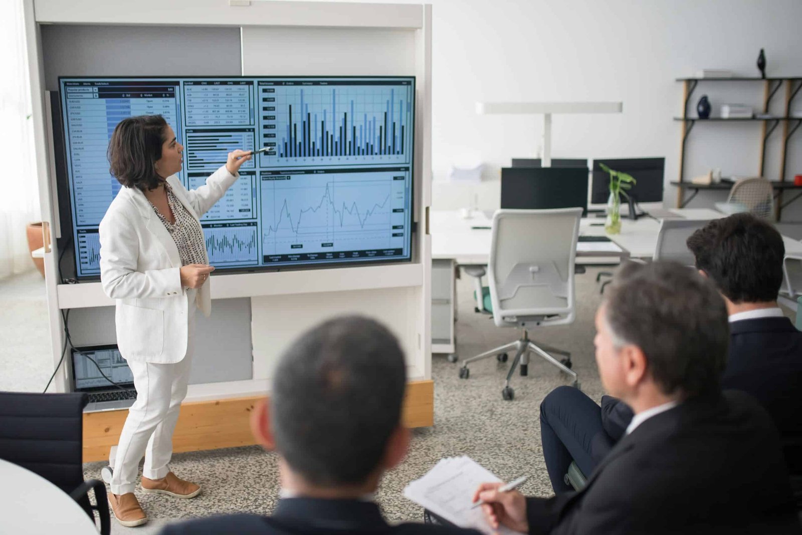 Businesswoman presenting graphs on a screen during a meeting about Strategic Planning vs Tactical Planning.